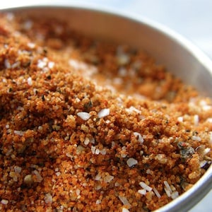 May include: Close-up of a bowl filled with a blend of spices, including red pepper flakes, salt, and black pepper.