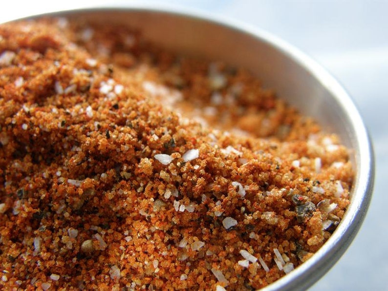 May include: Close-up of a bowl filled with a blend of spices, including red pepper flakes, salt, and black pepper.