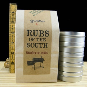 May include: A brown paper bag with the text "Rubs of the South" and "Barbecue Rubs" printed on it. The bag is next to a stack of silver metal containers.