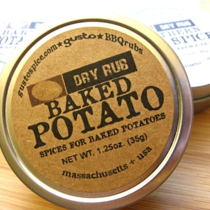 May include: A small, round, silver tin with a brown paper label. The label says "gustospice.com gusto BBQrubs Dry Rub Baked Potato Spices for Baked Potatoes Net Wt. 1.25oz. (35g) massachusetts + usa"
