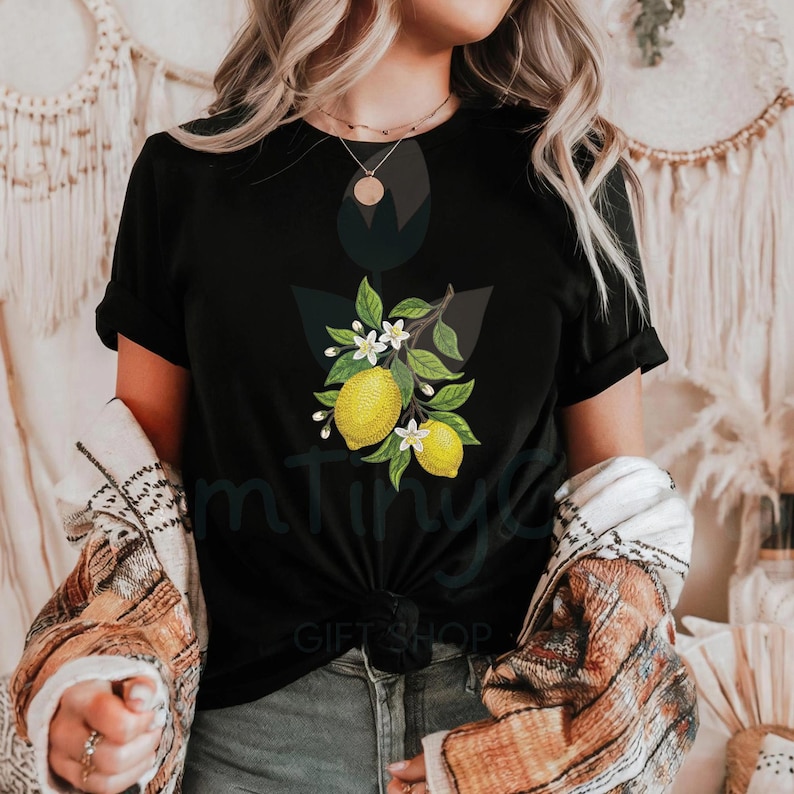 Puede incluir: Camiseta negra con un dise&ntilde;o de rama de lim&oacute;n. El dise&ntilde;o incluye limones amarillos, flores blancas y hojas verdes. La camiseta tiene mangas cortas y cuello redondo. El texto "mTiny GIFT SHOP" es visible en la parte inferior.