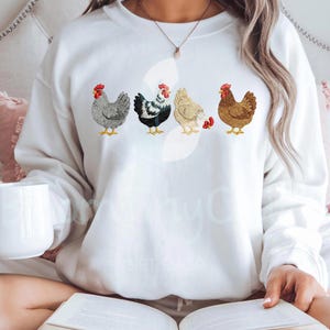 May include: White sweatshirt featuring embroidered chickens in various colors. The chickens have red combs and yellow feet. The sweatshirt is a comfortable, casual style, perfect for everyday wear. The design is centered on the front of the shirt.