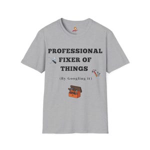 Könnte beinhalten: Hellgraues T-Shirt mit dem schwarzen Text "PROFESSIONELLER REPARATEUR VON DINGEN". Das Shirt zeigt Illustrationen von Werkzeugen und einer Werkzeugkiste. Darunter steht der Satz "(By Googling it)".