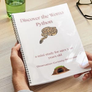 Puede incluir: Un libro encuadernado en espiral titulado "Discover the Woma Python" con una ilustración de serpiente. La portada también incluye el texto: "a mini study for ages 5-10 years old" y "Observation-Curiosity-Reflection". El libro está en manos de una persona.