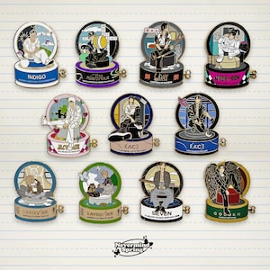 May include: A collection of enamel pins with various designs. Each pin features a circular scene with a figure, set atop a cylindrical base. The bases have text like "INDIGO", "JACK BOX", and "GOLDEN". The pins are detailed with vibrant colors and intricate designs.