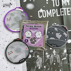 May include: Several round coasters featuring a cartoon bomb design in shades of grey, white, and black. Some coasters have a smiling face and the number 7. A blind bag labelled "Army Bomb" is also present.