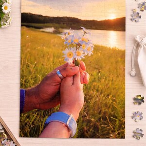 May include: Custom 120-piece puzzle, 8.27 x 11.69 inches, featuring a scenic image of a sunset over a field and water. The puzzle image shows a bouquet of white daisies held by two people. The puzzle pieces are scattered around.