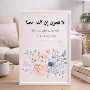May include: Framed art print with floral design and Arabic text. The print features a watercolour-style bouquet of pink, peach, and blue flowers. The English text reads "Do not grieve; indeed, Allah is with us."