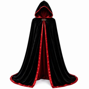 May include: A floor-length black velvet cloak featuring a deep red satin lining and trim. The garment includes an attached hood and a decorative metallic clasp at the neckline, creating a structured silhouette with a vibrant red border.