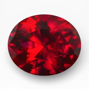 May include: A round, faceted ruby gemstone. The gem is a deep, vibrant red color with multiple facets that reflect light. The gemstone is set against a white background.