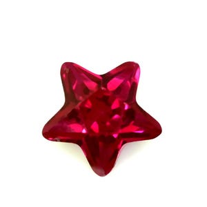 May include: A bright red, star-shaped gemstone with multiple facets. The five-pointed star has a glossy, reflective surface. The gem is set against a plain white background, emphasizing its shape and colour.