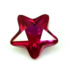 May include: A faceted, star-shaped gemstone in a vibrant ruby red hue. The gemstone has five points and a complex internal structure, reflecting light. The star's centre is a deeper shade of red, with white triangular facets. The gemstone is set against a white background.