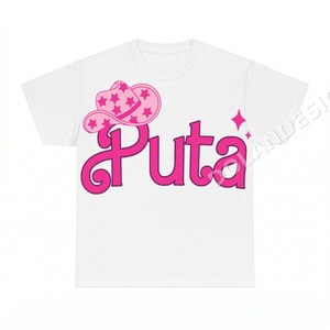 May include: A white short-sleeved t-shirt featuring a graphic print on the front. The design includes a pink cowboy hat decorated with stars, positioned above the word Puta in a bold, stylised pink font, accompanied by a small four-pointed star.