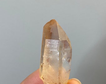 May include: A clear quartz crystal with a light brown hue. The crystal is pointed at both ends and has a natural, rough texture.