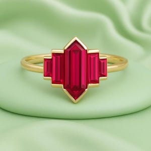May include: A gold ring featuring a geometric design with a vibrant red gemstone. The ring's band is a simple, polished gold, while the gemstone is a striking, multi-faceted shape, creating a bold and elegant statement piece.