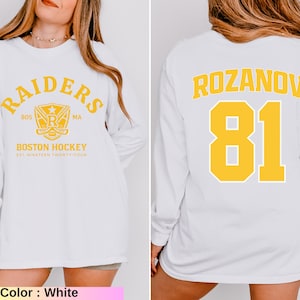 May include: White long-sleeve sweatshirt featuring "RAIDERS" and "BOSTON HOCKEY" text with a logo on the front. The back displays "ROZANOV 81" in yellow. The sweatshirt is a casual style, perfect for sports fans.
