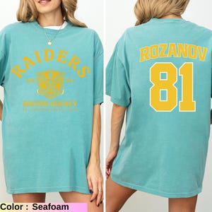 May include: Seafoam green t-shirt with "RAIDERS" arched text and a crest graphic on the front. The back features "ROZANOV" and the number "81" in yellow. The shirt is a comfortable, oversized fit.