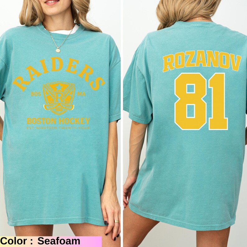 May include: Seafoam green t-shirt with "RAIDERS" arched text and a crest graphic on the front. The back features "ROZANOV" and the number "81" in yellow. The shirt is a comfortable, oversized fit.