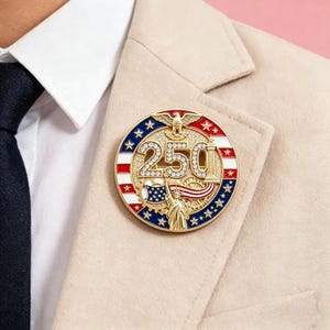 May include: A circular gold-tone lapel pin featuring the number 250 in clear rhinestones. The design includes a golden eagle at the top, the Statue of Liberty at the bottom, and a background of red, white, and blue stripes with white stars.