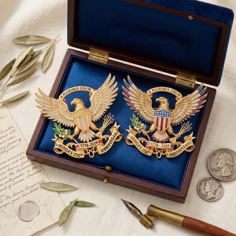 Pu&ograve; includere: Due spille a forma di aquila dorata in una scatola di legno foderata di blu. Ogni spilla raffigura un'aquila con ali spiegate, uno scudo e un nastro con la scritta E PLURIBUS UNUM e AMERICA'S 250TH ANNIVERSARY 1776-2026. Una &egrave; dorata, l'altra smaltata.