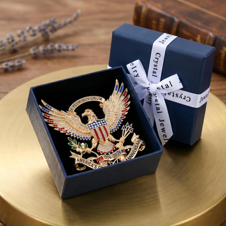 Pu&ograve; includere: Una spilla a forma di aquila color oro con smalto rosso, bianco e blu e cristalli trasparenti. L'aquila tiene frecce e un ramoscello d'ulivo, con un nastro che reca la scritta E PLURIBUS UNUM e AMERICA'S 250TH ANNIVERSARY 1776-2026, in una scatola blu.