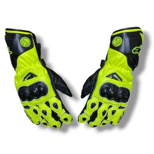 Könnte beinhalten: Ein Paar neongelbe und schwarze Motorradhandschuhe. Die Handschuhe haben einen schwarzen Schutzpanzer an Knöcheln und Handgelenk. Der Text "GP PRO" ist auf dem Handgelenk aufgedruckt. Sie haben einen Klettverschluss für einen sicheren Sitz.