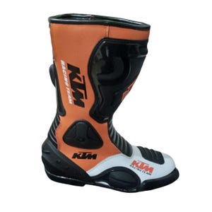 Könnte beinhalten: Orangener und schwarzer Motorradstiefel mit weißen Akzenten. Der Stiefel zeigt das KTM Racing Team Logo. Er hat ein hohes Design mit Schutzplatten und einer robusten Sohle.
