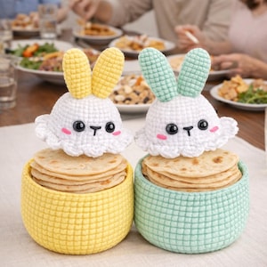 May include: Two crochet bunny-shaped tortilla warmers. One is yellow, the other is mint green. Each has a white head with black eyes, pink cheeks, and a stack of tortillas inside. The bunny ears are yellow and mint green.