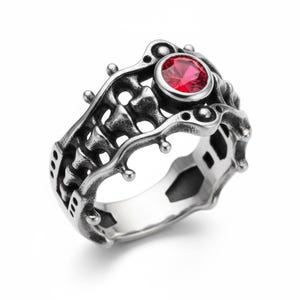 Op de afbeelding: Een zilverkleurige ring met een ingewikkeld, opengewerkt ontwerp. De ring heeft een prominente, ronde, rode edelsteen. De band heeft een gedetailleerd, getextureerd patroon met kleine, afgeronde accenten. De stijl is gotisch of fantasy-geïnspireerd.
