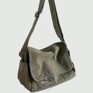 Könnte beinhalten: Olivgrüne Umhängetasche mit Klappenverschluss und verstellbarem Schultergurt. Die Tasche hat eine Seitentasche und eine Cordstruktur. Die Tasche hängt vor einem weißen Hintergrund.
