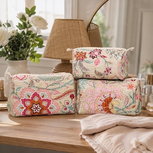 Peut inclure: Trois trousses matelassées rectangulaires avec une base beige et un motif floral vibrant dans des tons de rose, orange, bleu sarcelle et vert. Chaque trousse possède une fermeture éclair sur le dessus et une forme structurée avec des coutures.