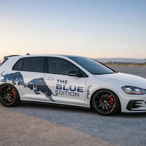 Op de afbeelding: Witte hatchback auto met zwarte velgen en rode remklauwen. De auto heeft een blauwe afbeelding van twee stieren en de tekst "THE BLUE EDITION". De auto staat geparkeerd op een verharde ondergrond.