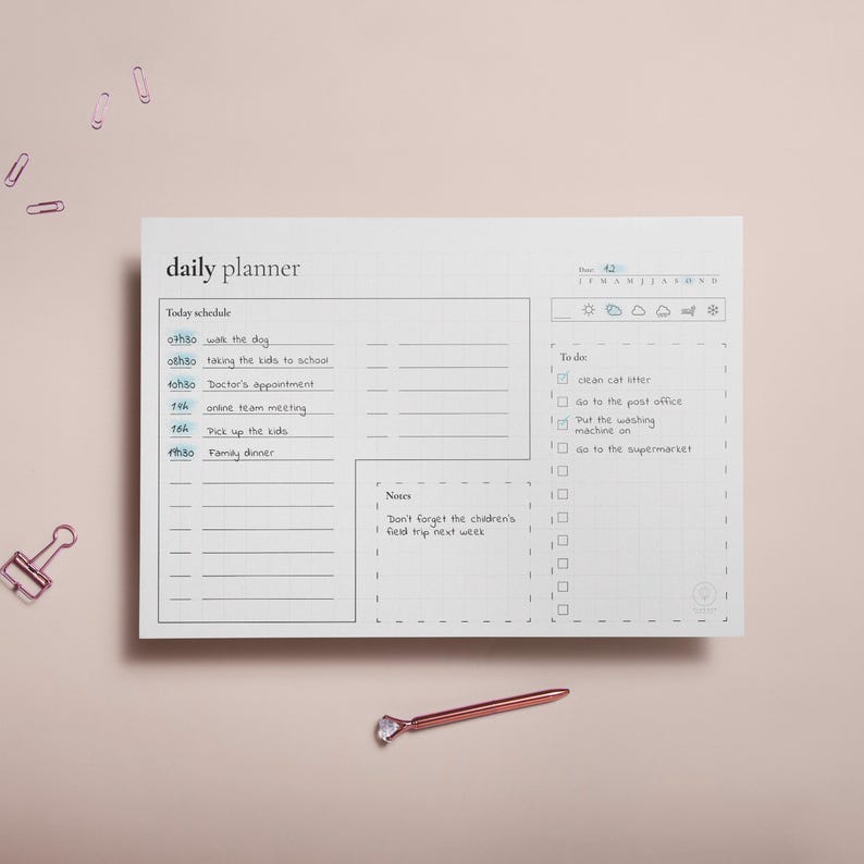 Puede incluir: Un planificador diario blanco con un patr&oacute;n de cuadr&iacute;cula, con un horario y una lista de tareas. El horario incluye horarios y actividades como "pasear al perro" y "cena familiar". Un bol&iacute;grafo y clips de papel de oro rosa est&aacute;n sobre un fondo rosa.