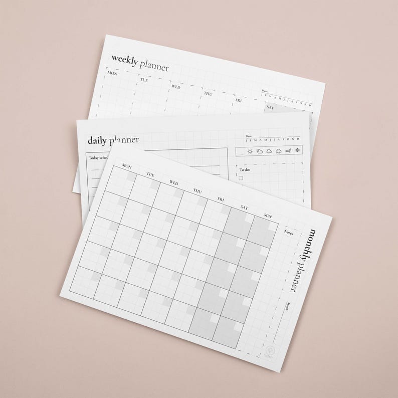 Puede incluir: Una pila de planificadores de papel blanco, que incluyen un planificador semanal, diario y mensual. Los planificadores tienen un dise&ntilde;o de cuadr&iacute;cula con secciones para fechas, notas y listas de tareas. Los textos "weekly planner", "daily planner" y "monthly planner" son visibles.