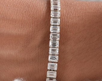 May include: A tennis bracelet featuring a continuous row of clear, emerald-cut stones set in a metallic band. The stones are rectangular in shape and arranged vertically along the length of the bracelet, creating a uniform and reflective appearance.