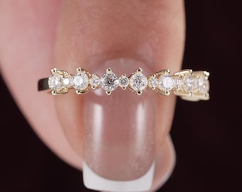 May include: A gold band ring featuring a series of alternating large and small round clear stones set in a horizontal row. The metal band has a polished finish and the stones are arranged in a repeating pattern across the front of the ring.