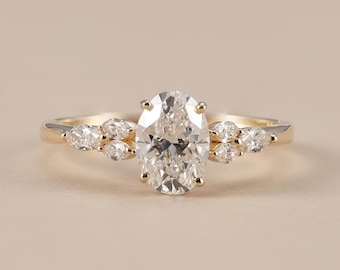 May include: A gold ring featuring a large central oval-cut diamond held by four prongs. The band is accented on each side by a cluster of three smaller marquise-cut diamonds, creating a symmetrical arrangement along the polished gold metal band.