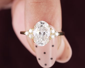 May include: A gold ring featuring a large oval-cut centre stone flanked by three smaller round-cut stones on each side. The setting is crafted from polished yellow gold, showcasing a classic multi-stone design with a prominent central gemstone.