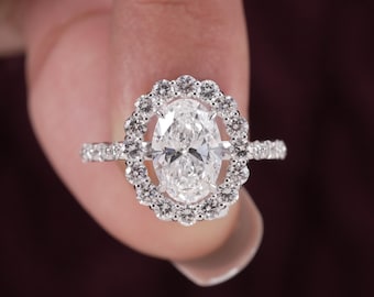 May include: A silver-coloured ring featuring a large oval-cut centre stone surrounded by a scalloped halo of small round stones. The band is thin and encrusted with additional small round stones along the visible sides of the setting.