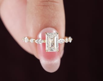 May include: A gold ring featuring a central emerald-cut gemstone flanked by smaller marquise-cut and round-cut stones along the band. The setting is crafted from polished yellow gold, highlighting the clear, faceted stones in a linear arrangement.