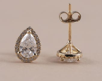 May include: A pair of gold stud earrings featuring a central pear-shaped clear stone surrounded by a halo of smaller clear stones. One earring is shown from the front, while the other is shown from the back, displaying the post and clutch.
