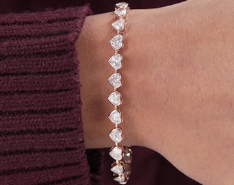 May include: A rose gold-toned bracelet featuring a continuous row of linked heart-shaped clear stones. Each stone is set within a metallic frame, creating a uniform chain design that wraps around the wrist with a polished and reflective finish.