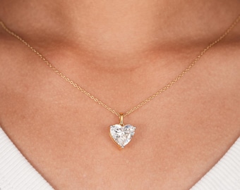 May include: A gold chain necklace featuring a heart-shaped pendant with a clear, faceted stone set in a gold frame. The pendant hangs from a delicate gold link chain that rests against the neck, showcasing a classic design with a polished finish.