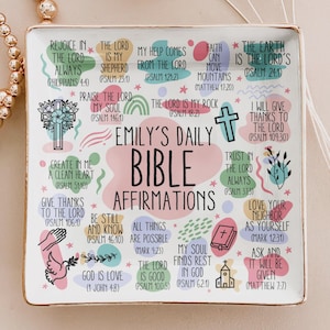 Könnte beinhalten: Ein quadratisches, weißes Dekotablett mit goldenem Rand, das den Text "Emily's Daily Bible Affirmations" trägt. Das Tablett ist mit verschiedenen inspirierenden Sätzen und Bibelversen in schwarzem Text mit farbenfrohen Pastellakzenten verziert.