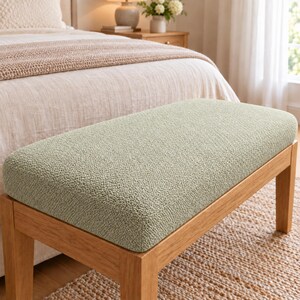 May include: A rectangular bench featuring a light sage green textured fabric upholstered seat supported by four sturdy wooden legs with a natural light brown finish. The bench has a clean, simple design with rounded corners on the seat cushion.