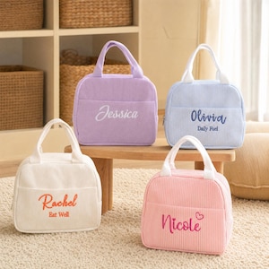Puede incluir: Cuatro bolsas de almuerzo de pana con asas superiores y bolsillos frontales. Las bolsas son de color lavanda con 'Jessica', azul claro a rayas con 'Olivia Daily Fuel', crema con 'Rachel Eat Well' y rosa a rayas con 'Nicole' bordados.