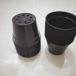 以下が含まれることがあります： 黒いプラスチック製の植木鉢の積み重ねと、その横に置かれた単一の黒いプラスチック製の植木鉢。積み重ねられた方は逆さまになっており、複数の排水穴がある底面が見えています。もう一方の鉢は直立しており、広い円形の縁が開いています。