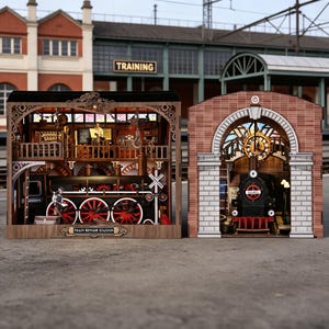 以下が含まれることがあります： 2つの詳細な木製鉄道模型。1つは蒸気機関車のある列車修理ステーション、もう1つは時計と蒸気機関車のある駅です。モデルは茶色、黒、赤で、複雑なディテールが施されています。