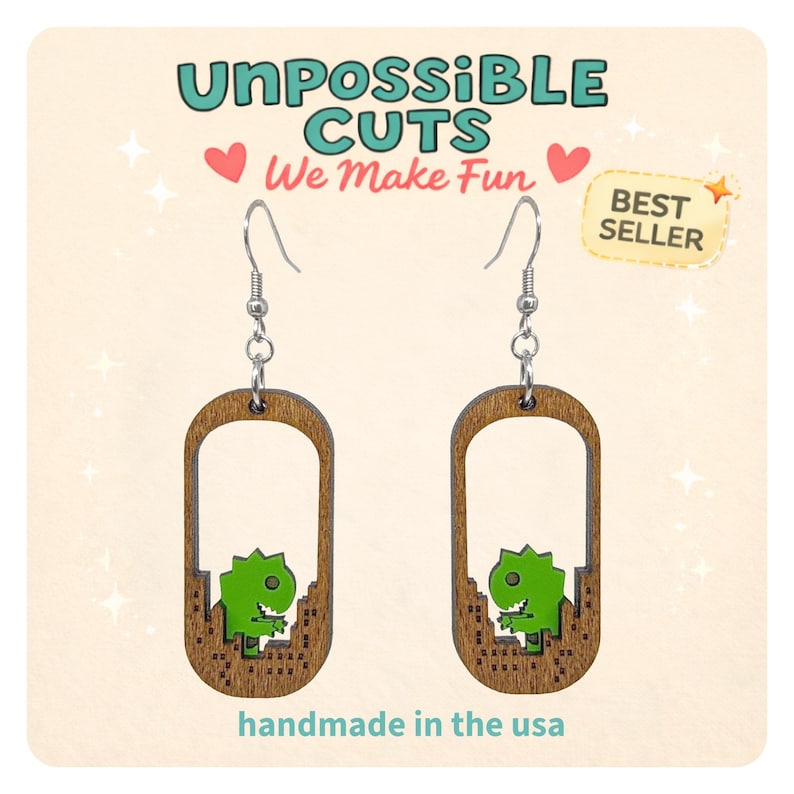 May include: Wooden earrings with a dinosaur design. The earrings are brown with a green dinosaur and the text "UnPossible Cuts We Make Fun" and "handmade in the usa". The earrings are a best seller.