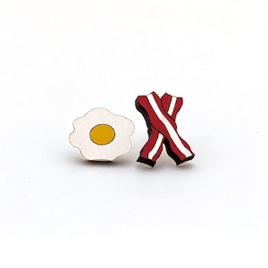 May include: Wooden cutout of a fried egg and bacon, both in red, white, and yellow colors.